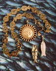 Stylized shot featuring the strong rainbow fish pendant, strong carved mother of pearl fish, strong enduring sun, and the strong pesce d'oro chain, all on a photograph of a school of fish