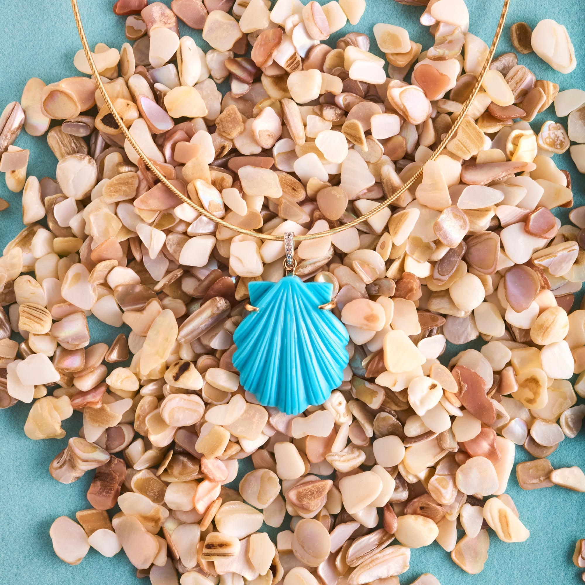 Stylized shot of the carved turquoise shell on the omega wire on a bed of shell pieces