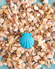 Stylized shot of the carved turquoise shell on the omega wire on a bed of shell pieces