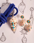 Stylized shot of the strong in the shallows shell pendant and strong soaking up the sun earrings. Shown with knotted blue rope and background of seashell drawings