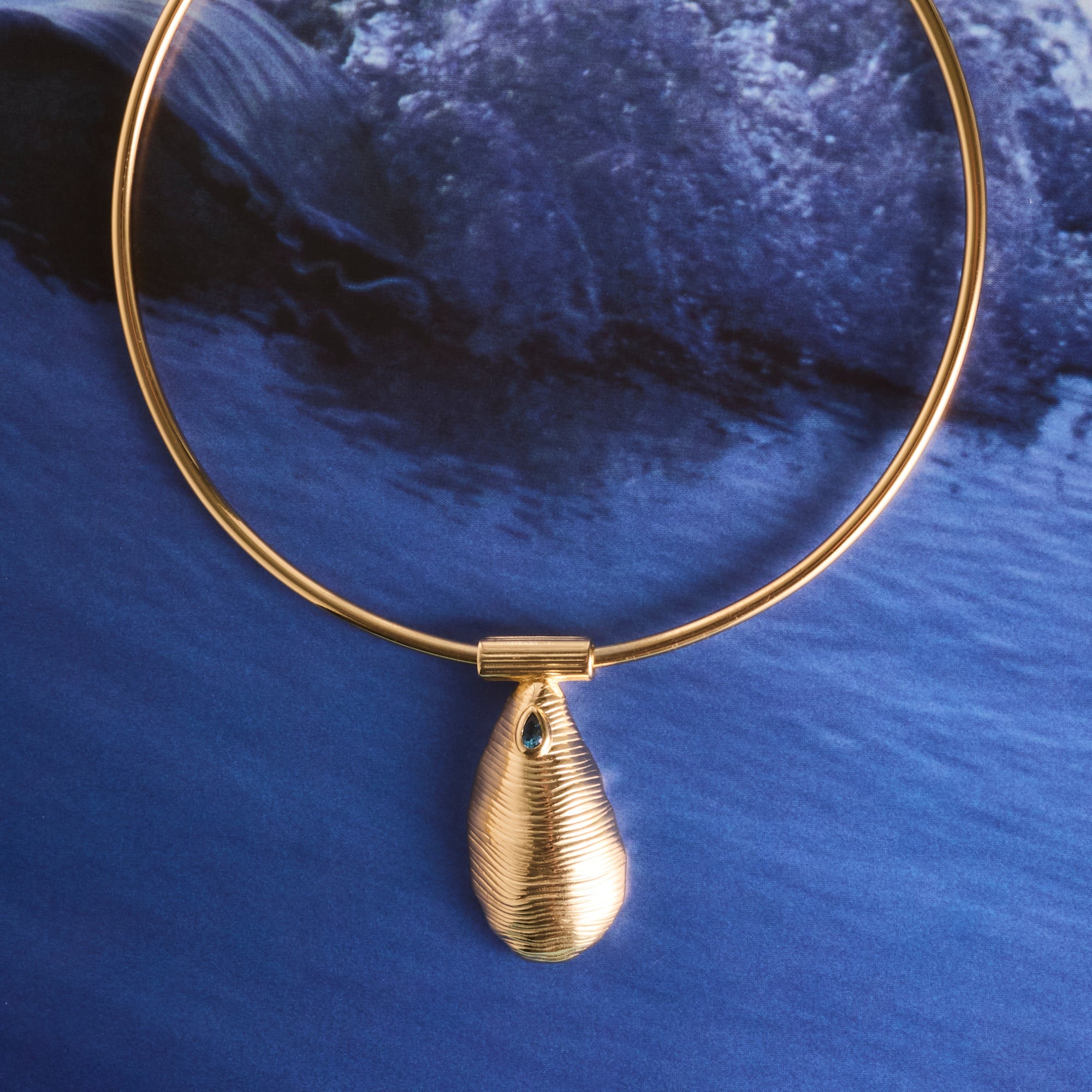 Stylized shot of the strong along the shore pendant on the neck cuff on a photo of a wave crashing