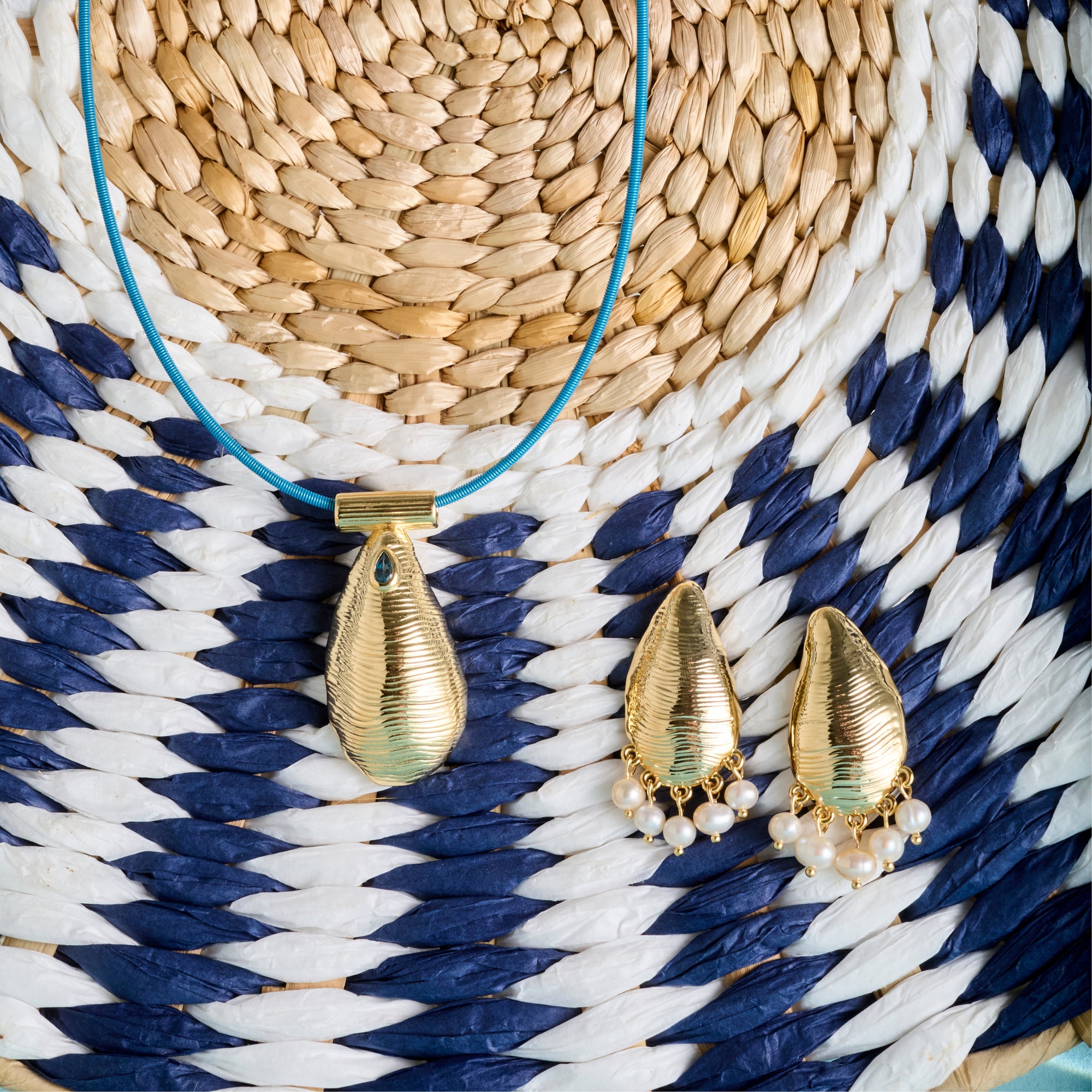 Stylized shot of the strong along the shore earrings and strong along the shore pendant on the blue omega wire. Shown on a blue and white woven basket