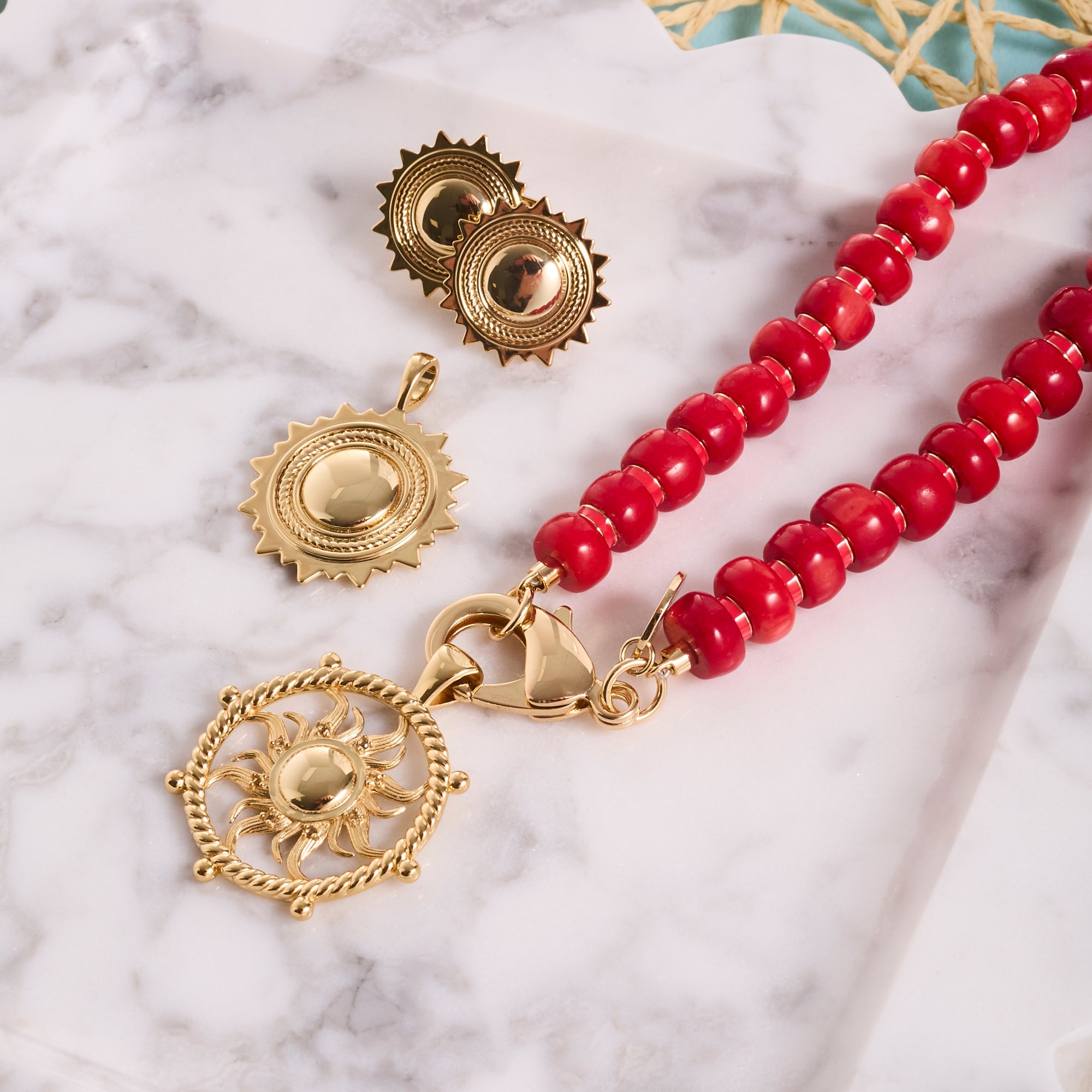 Stylized shot of sun pendants, sun earrings, and coral beaded necklace on a marble tray