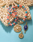Stylized shot of protect gleaming eye, protect evil eye petite embellished, protect with my eye on you, and turquoise and coral gumdrop necklace