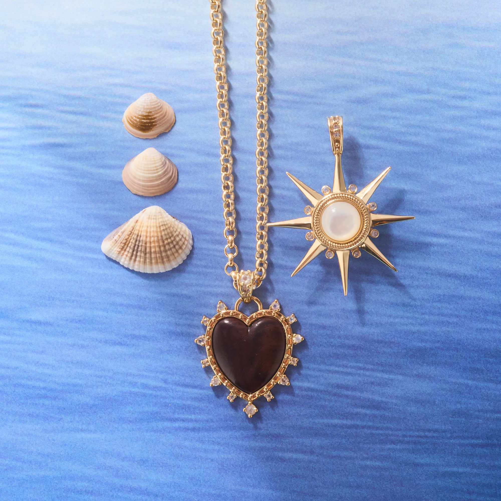 Stylized shot of the love dolce carved heart on the grand rolo chain and the strong supernova pendant in mother of pearl. Shown with seashells and ocean inspired background.
