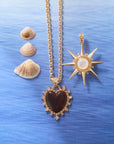 Stylized shot of the love dolce carved heart on the grand rolo chain and the strong supernova pendant in mother of pearl. Shown with seashells and ocean inspired background.