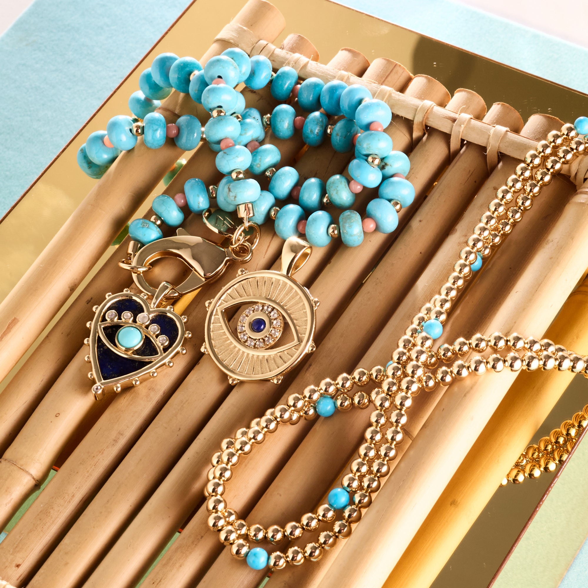Stylized shot of the turquoise and coral beaded necklace, turquoise and gold bead double wrap, protect with an open eye pendant and protect queen of hearts pendant