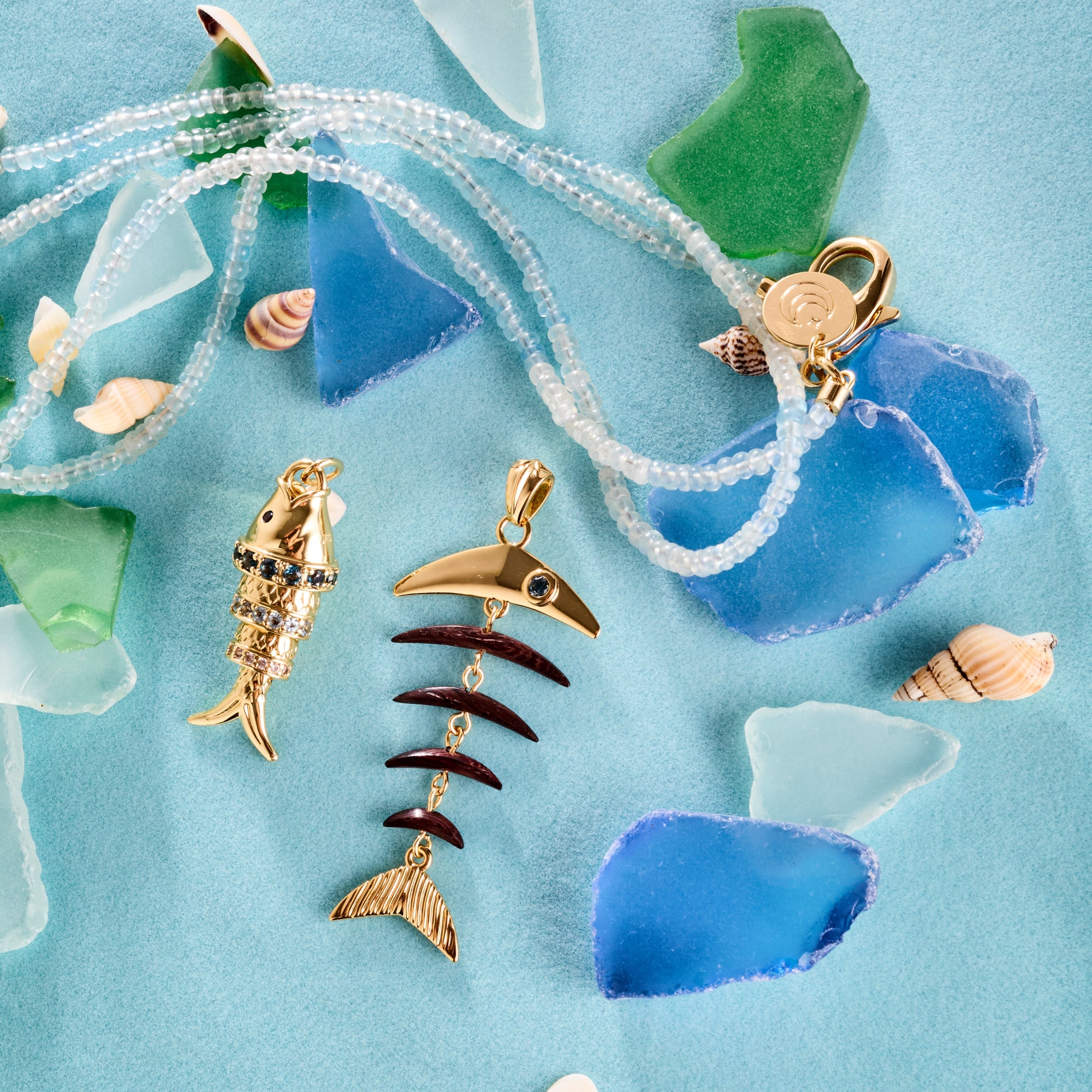 Stylized shot of strong fishbone pendant, strong rainbow fish pendant, double wrap in aquamarine on turquoise background with seaglass pieces
