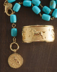 Stylized shot of chunky turquoise lariat with the courage year of the horse coin and the courage run with horses cuff