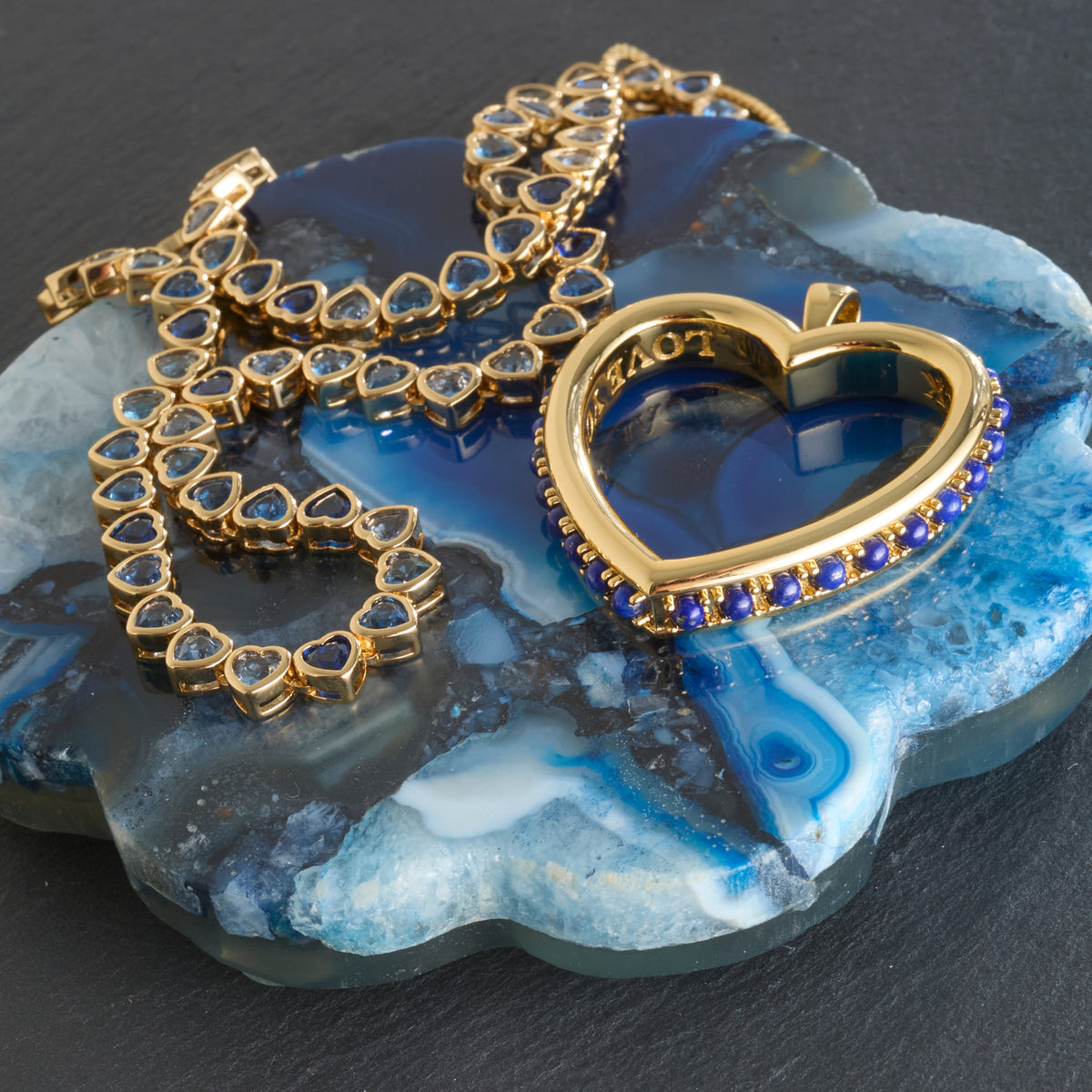 Stylized shot of the love you to the moon and back heart and made from love tennis necklace on a slice of blue agate