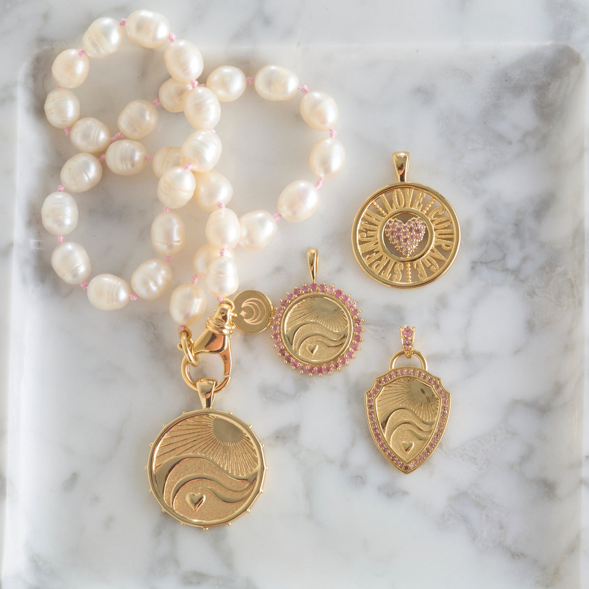 Stylized shot of the pendants from the love courage strength collection with the white pearl knotted necklace on a marble background