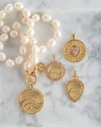 Stylized shot of the pendants from the love courage strength collection with the white pearl knotted necklace on a marble background