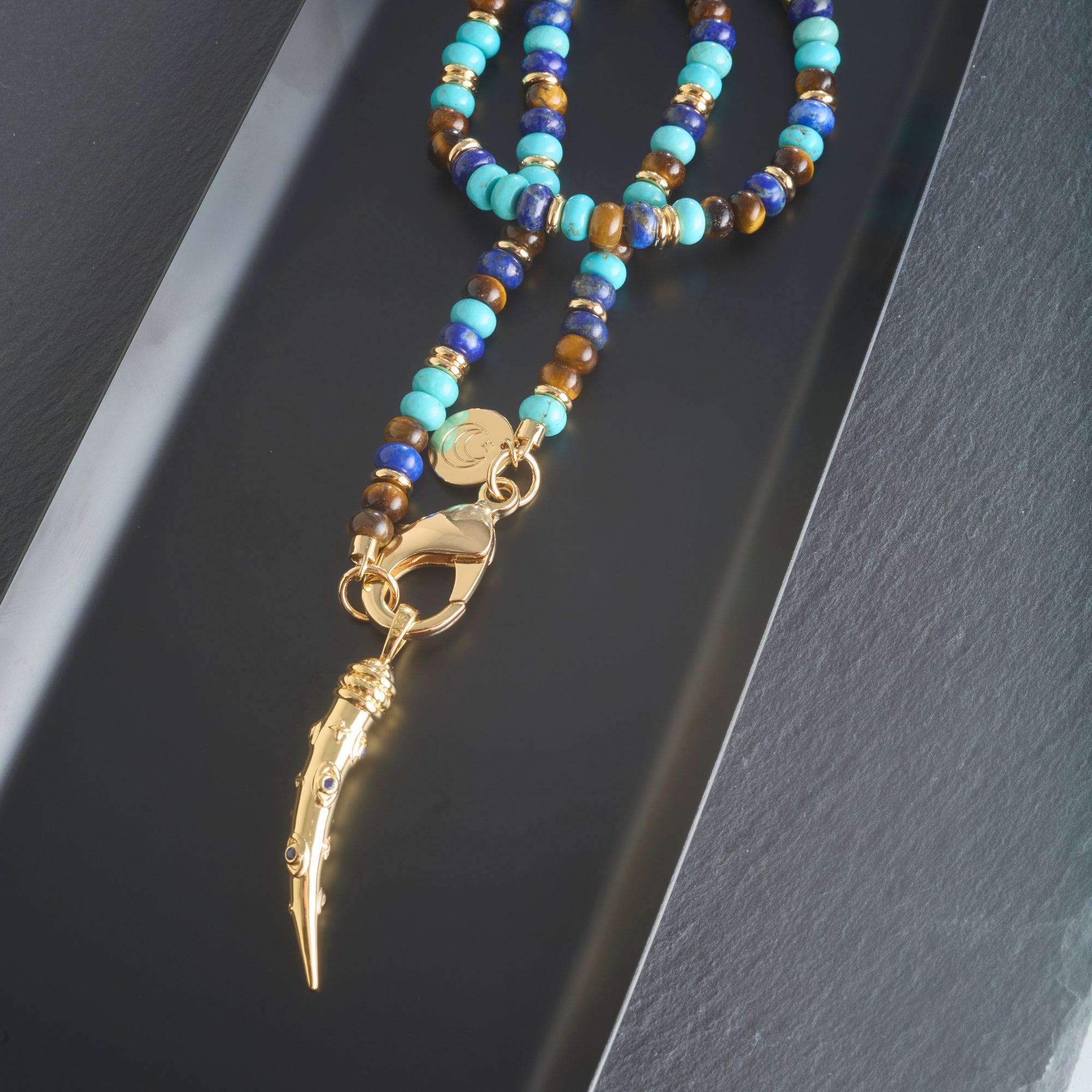 Stylized shot of the protect ancient eye tusk pendant on the shoreline mix gumdrop beaded necklace.