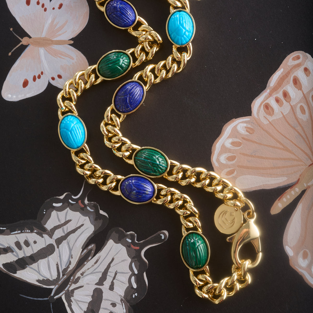 Stylized shot of the protect scarab curb chain with a painting of butterflies