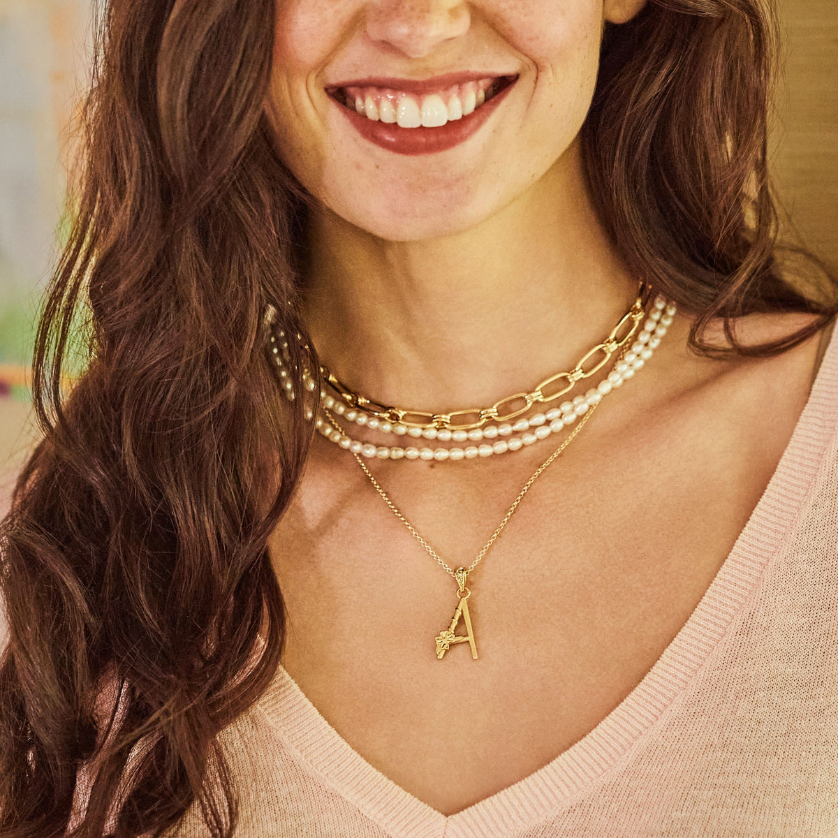 Model wearing the wheels of fortune chain, pearl double wrap, and the dogwood letter A pendant