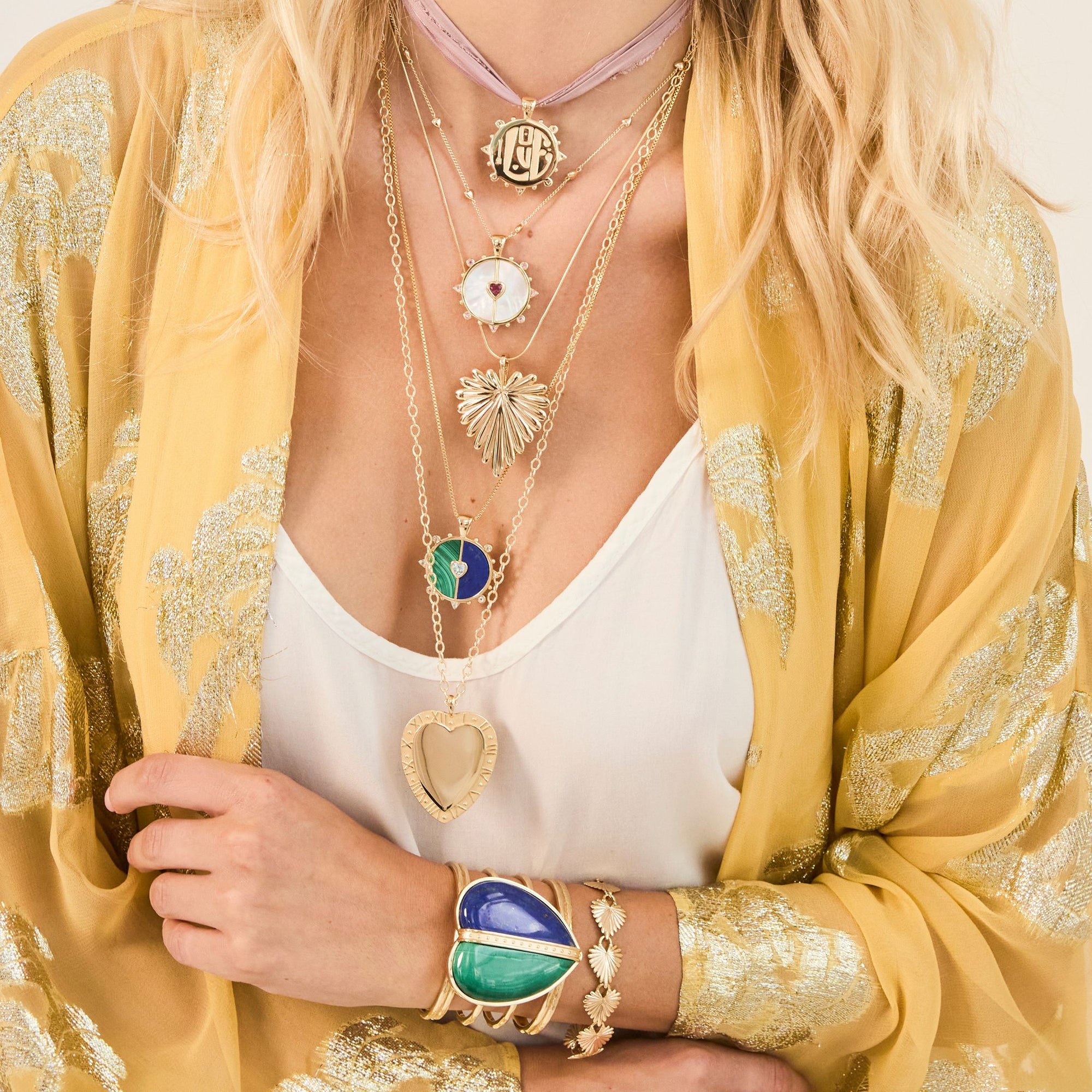 Woman wearing five heart necklaces, a heart cuff bracelet with two stones, and a heart chain bracelet.