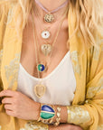 Woman wearing five heart necklaces, a heart cuff bracelet with two stones, and a heart chain bracelet.