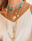 Model wearing layered gold and turquoise pendants