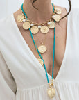 Model wearing various gold coins and long turquoise beaded necklace