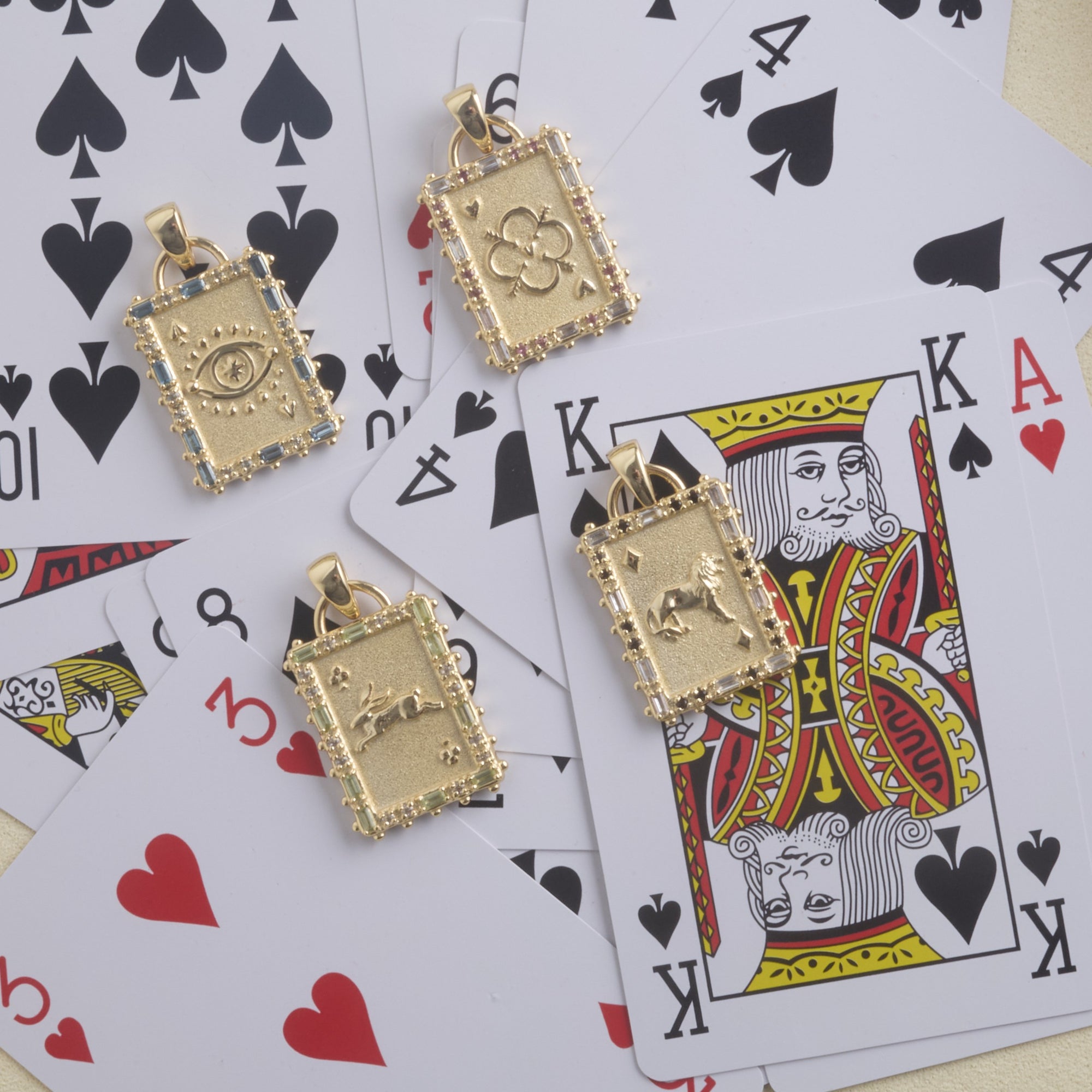 Stylized shot of each of the 4 playing card pendants on top of a pile of playing cards