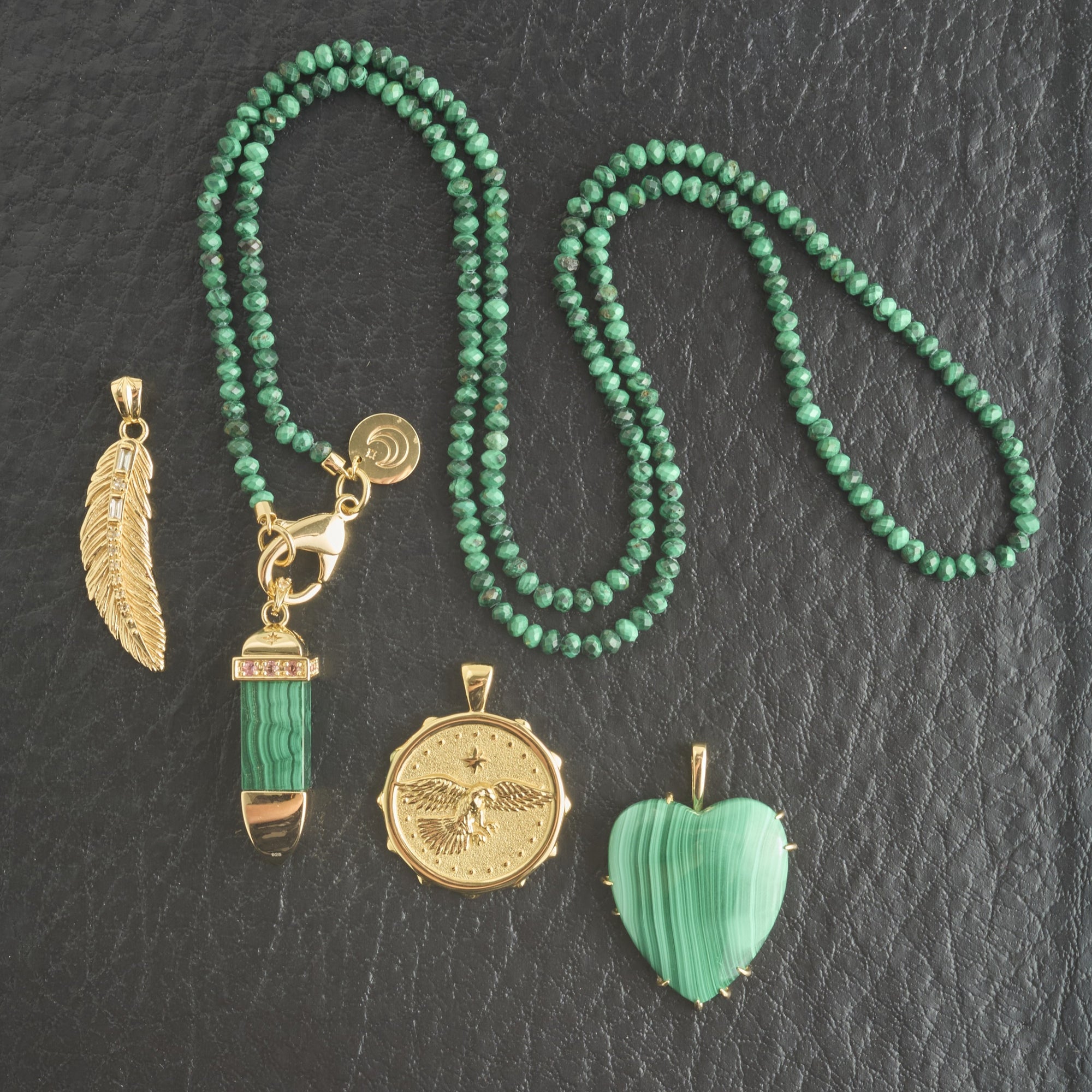 Stylized shot of lucky feather pendant, eagle coin, malachite sun ray, malachite heart, and malachite beaded chain