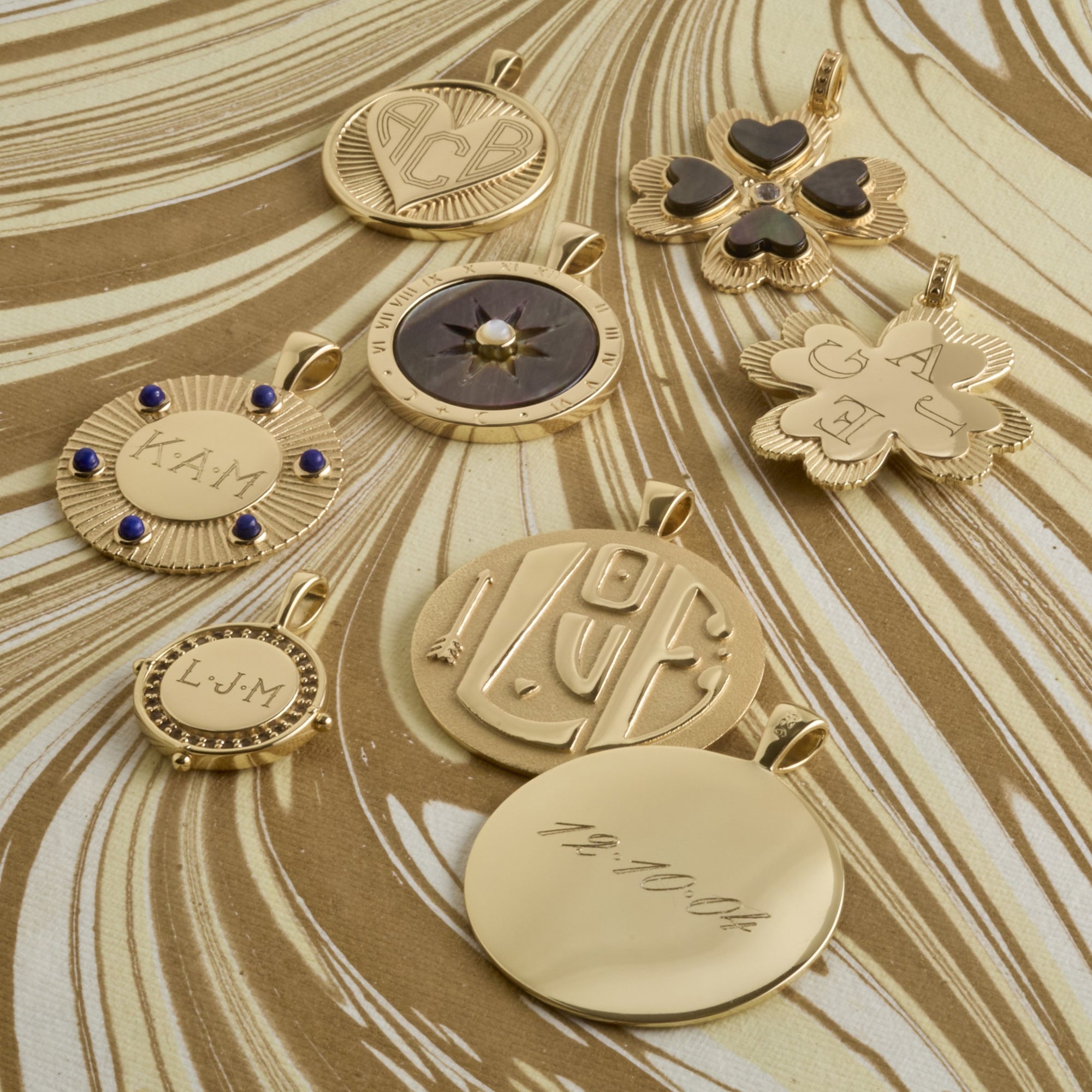Stylized shot of engravable pendants with sample engravings laid out on gold marbled background