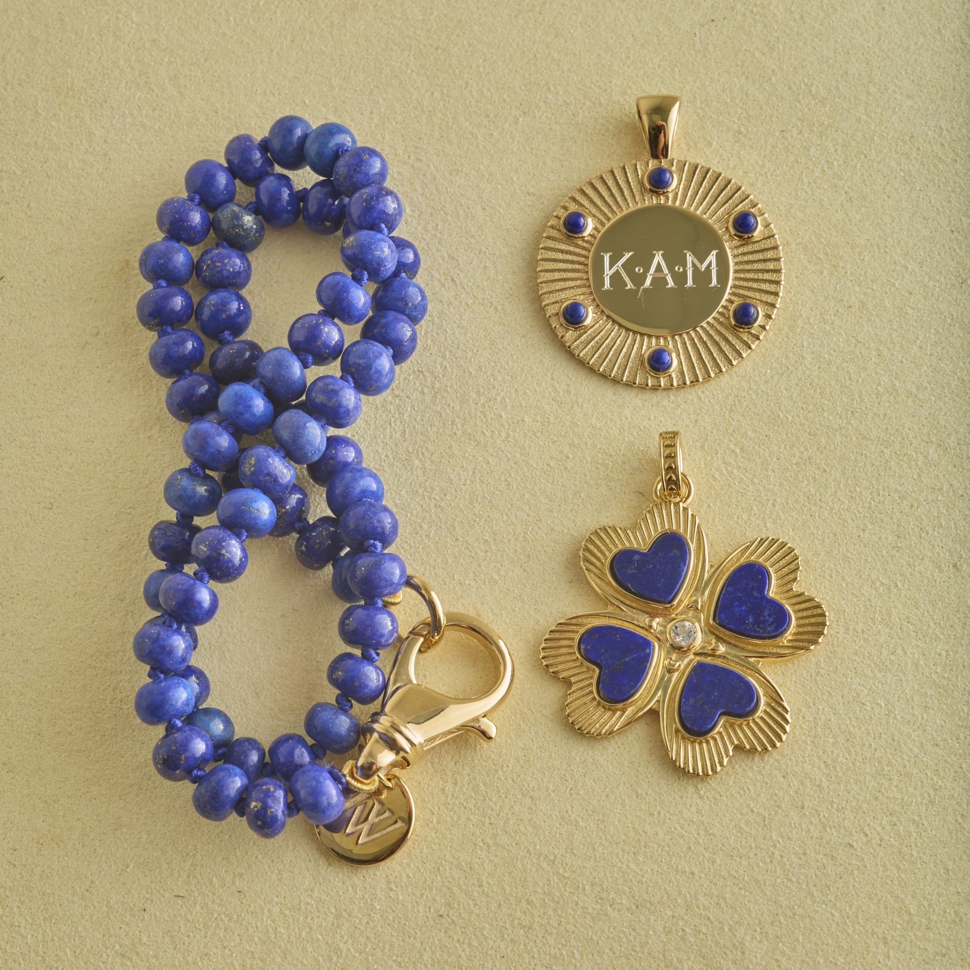 Stylized shot of beaded lapis chain and engraved forever around the sun pendant, and lapis clover pendant
