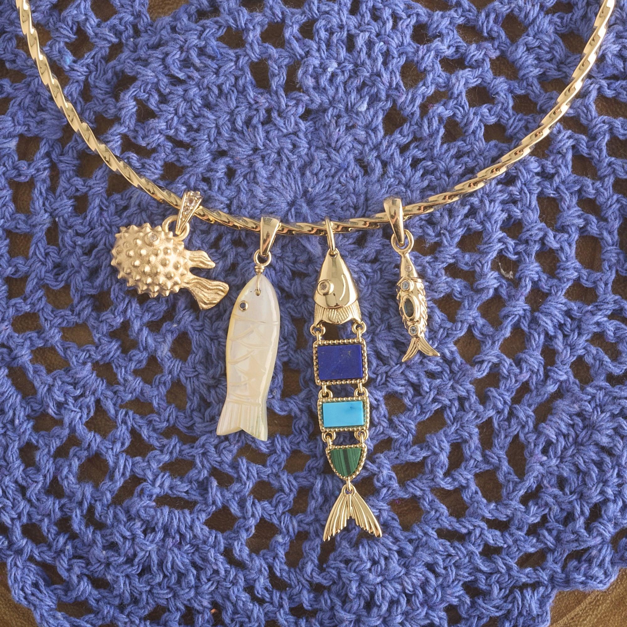 Stylized shot of various fish pendants on the twisted neck cuff laid out on blue crochet background
