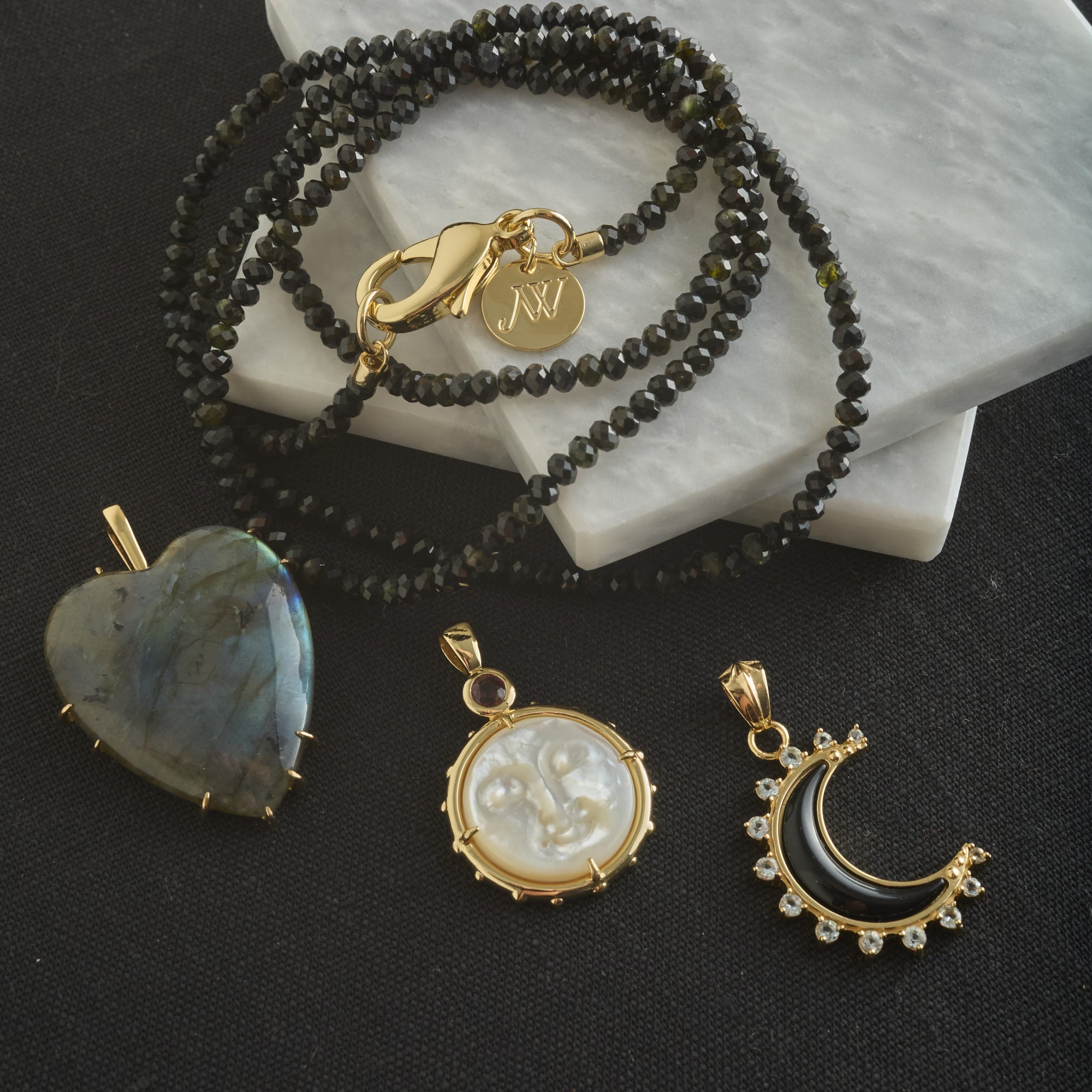 Stylized shot of labradorite heart pendant, mother of pearl moon face pendant, and onyx crescent moon pendant with black beaded necklace