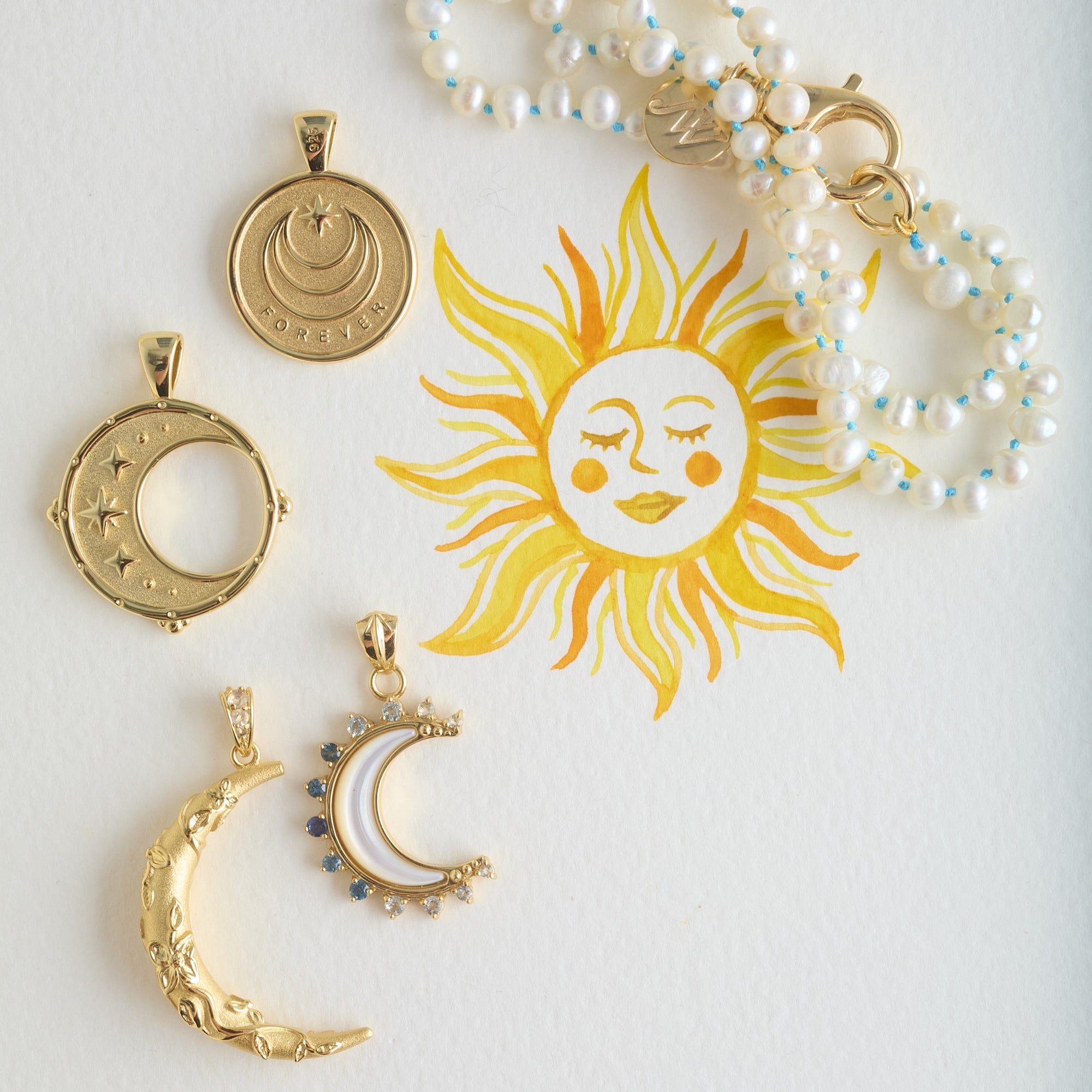 Stylized shot of moon pendants and pearl necklace with watercolor sun painting