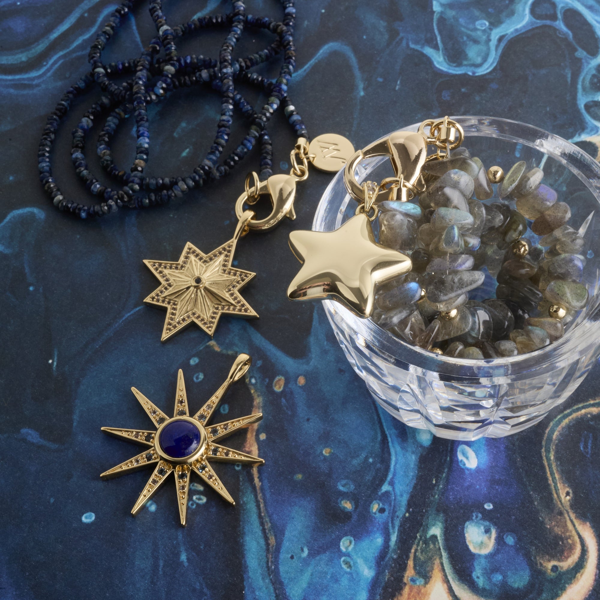 Stylized shot of star pendants, labradorite natural beaded necklace, and kyanite double wrap necklace on blue marbled background