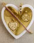 Stylized shot of the queen of hearts coin pendant, heart ray pendant, love in the air heart pendant, and made from love tennis bracelet in gold heart dish
